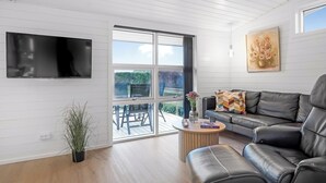 Ein modernes Wohnzimmer mit Flachbildfernseher, schwarzem Ledersofa, Couchtisch aus Holz und einer Topfpflanze.