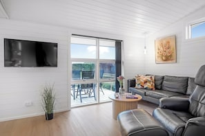 Una sala de estar moderna con un televisor de pantalla plana, un sofá de cuero negro, una mesa de centro de madera y una planta en maceta.