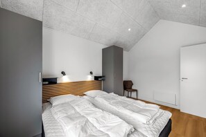 A modern bedroom with a sloped ceiling, a bed with white bedding, a wooden headboard, and a chair. - Lovely holiday apartment from 2026 in Søndervig, close to the North Sea. (Ringkøbing)