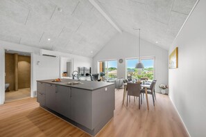A modern kitchen with a central island, a dining area with a view, and a large window. - Lovely holiday apartment from 2026 in Søndervig, close to the North Sea. (Ringkøbing)