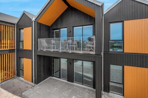 A modern multi-story building with a balcony, large windows, and a combination of dark and light wood paneling. - Lovely holiday apartment from 2026 in Søndervig, close to the North Sea. (Ringkøbing)