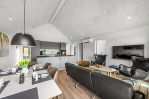 Eine moderne Küche mit Essbereich, ein Wohnbereich mit Fernseher und eine gemütliche Sitzecke mit Hundebett.