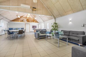 En rummelig opholdsstue med højt til loftet, et spisebord, sofaer og en trappe.
