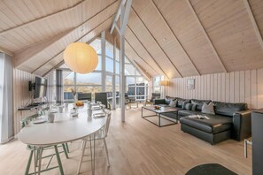 Ein geräumiges Zimmer mit hoher Decke, einem Esstisch mit Stühlen, einer Couch und einem Fernseher.
