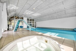 Une piscine intérieure avec un toboggan, un jacuzzi et un sol carrelé.