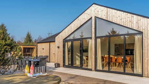 Ein modernes Holzgebäude mit großen Glasfenstern, Außenplätzen und einer Terrassenanlage.
