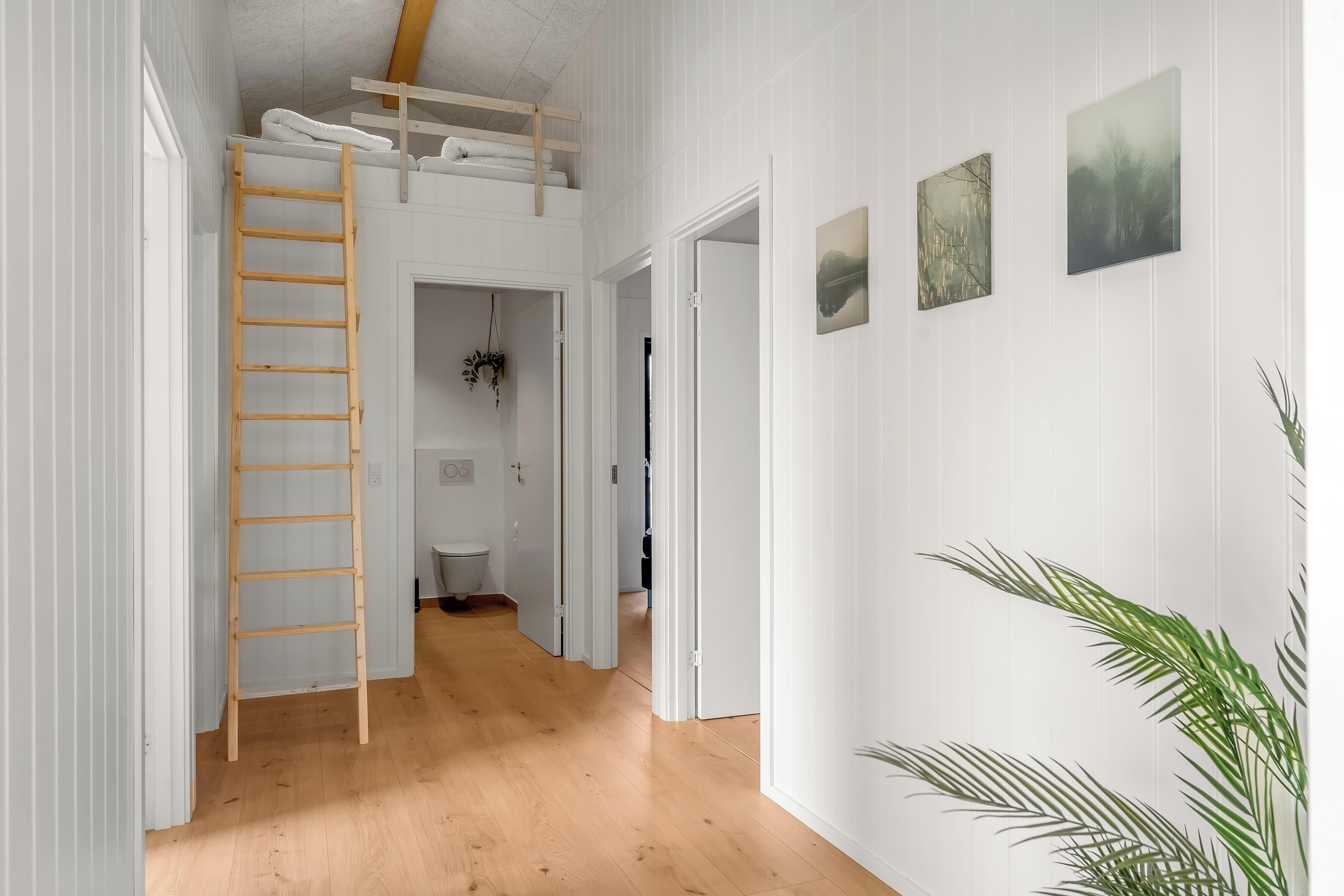 A narrow hallway with a wooden ladder, white walls, and a wooden floor.