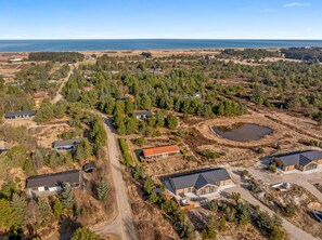 An aerial view of a residential area with houses, a pond, and a forested landscape. - Lovely 16-person luxury house with activity room, outdoor hot tub and outdoor. (Fjerritslev)