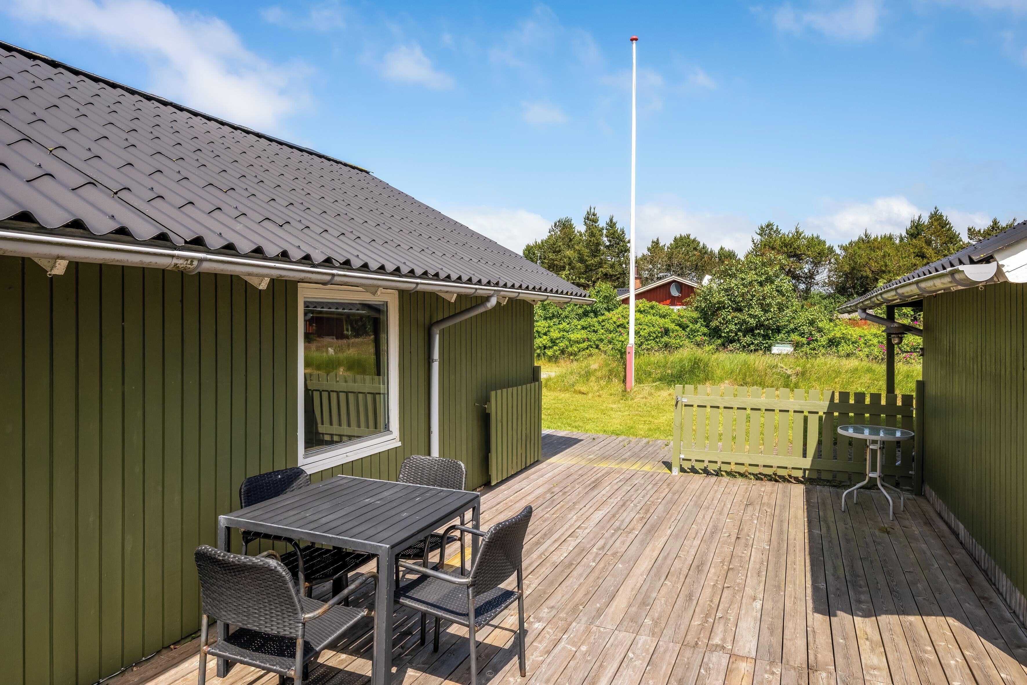 A wooden deck with a table and chairs, a small table, and a green building with a metal roof.