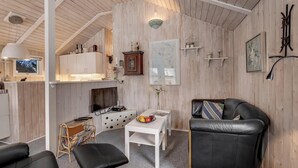 A cozy room with a wooden ceiling, a white table with fruit, a black leather sofa, and a television. - Well-maintained holiday home close to Ringkøbing Fjord. (Skjern)