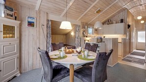 A dining area with a round table, chairs, and a kitchen in the background. - Well-maintained holiday home close to Ringkøbing Fjord. (Skjern)