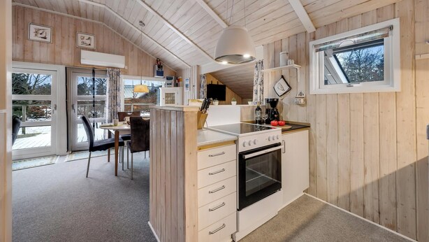 A kitchen with wooden walls, a stove, a sink, and a dining area with chairs and a table. - Well-maintained holiday home close to Ringkøbing Fjord. (Skjern)