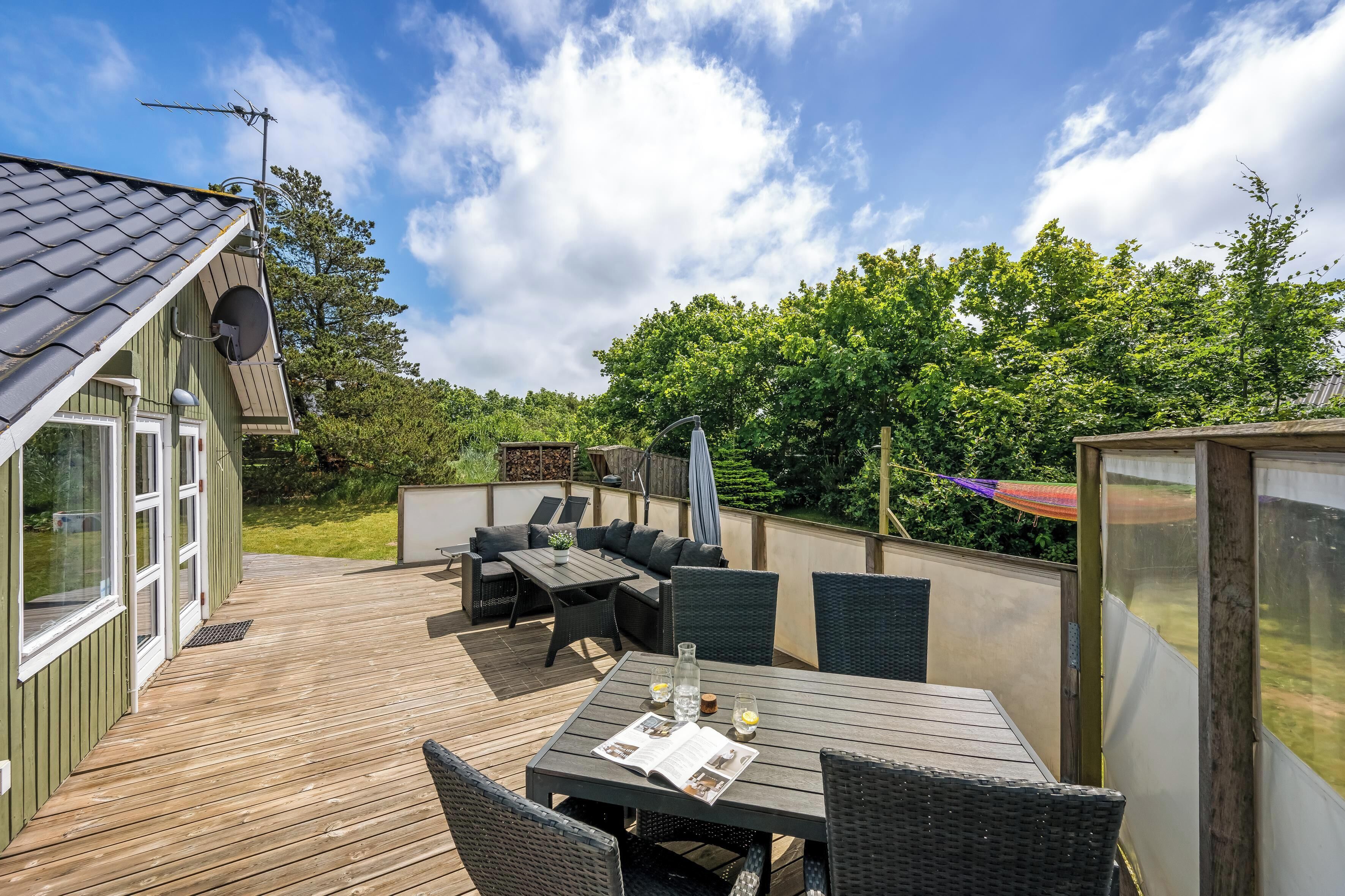 A wooden deck with outdoor furniture, a satellite dish, and a glass enclosure.