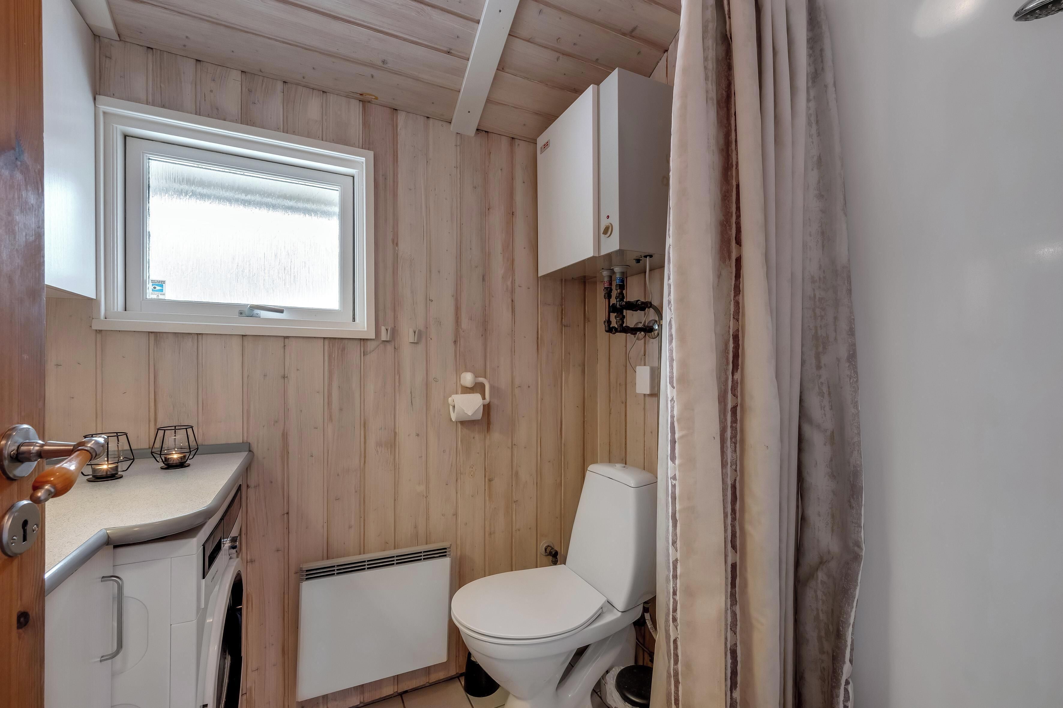 Une salle de bain aux murs lambrissés, équipée de toilettes, d’une fenêtre, d’un lavabo et d’un meuble de rangement.
