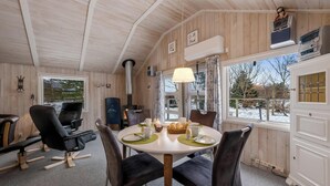 A wooden interior with a round dining table, chairs, a fireplace, and a view through a window. - Well-maintained holiday home close to Ringkøbing Fjord. (Skjern)
