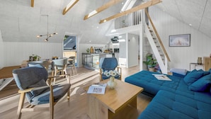 Ein Loft-Wohnraum mit hohen Decken, freiliegenden Holzbalken, einem Essbereich mit modernen Möbeln, einer Küche und einer Treppe, die in einen oberen Bereich führt.