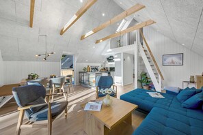 Ein Loft-Wohnraum mit hohen Decken, freiliegenden Holzbalken, einem Essbereich mit modernen Möbeln, einer Küche und einer Treppe, die in einen oberen Bereich führt.