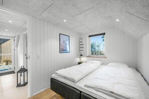 A bedroom with a bed, a window, a door, and a small table with a lamp. - Lovely holiday home built in 2025, with space for 8 people close to the North. (Ringkøbing)