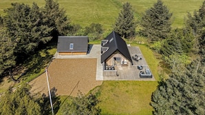 Ein modernes Haus mit einer großen Terrasse, umgeben von Feldern und Bäumen.