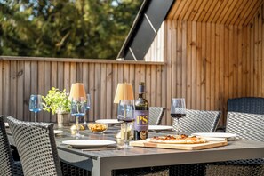 An outdoor dining area with wicker chairs, a table set with plates, glasses, a bottle, and a pizza. - Lovely holiday home built in 2025, with space for 8 people close to the North. (Ringkøbing)