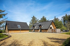 A modern building with a gravel driveway, wooden exterior, and a number '54' sign. - Lovely holiday home built in 2025, with space for 8 people close to the North. (Ringkøbing)