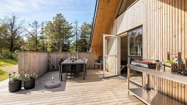 Eine Terrasse im Freien mit Esstisch, Stühlen, Grill und Holzzaun.