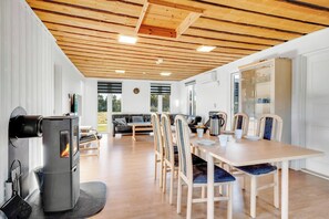 Ein modernes Interieur mit Kaminofen, Esstisch mit Stühlen, einer Couch und einem großen Fenster.