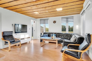 A modern living room with a wooden ceiling, a flat-screen TV, leather sofas, and a coffee table.