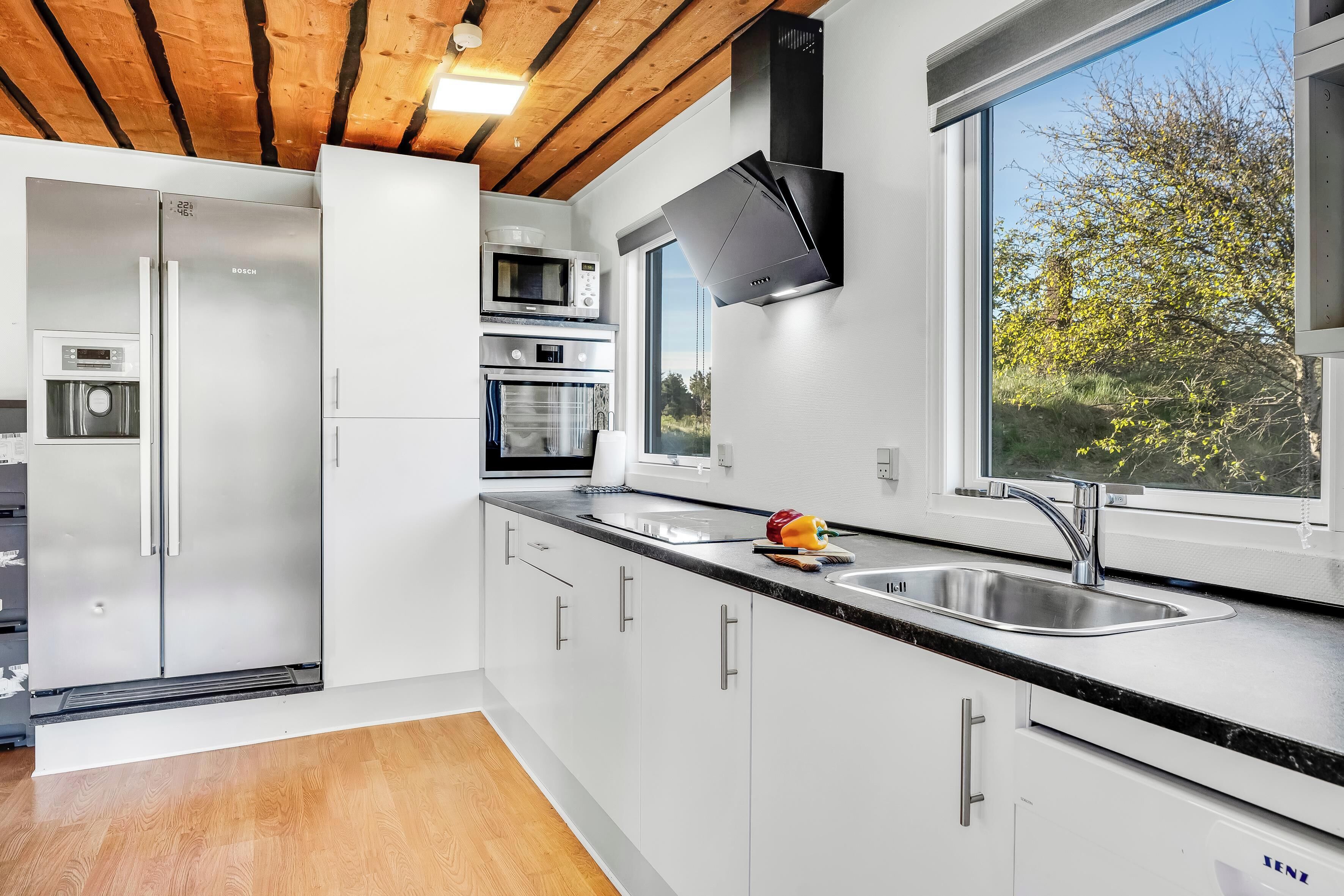 A modern kitchen with stainless steel appliances, a large window, and a wooden ceiling.