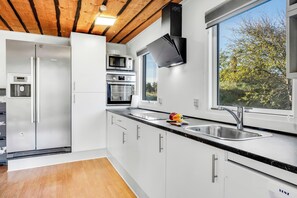 A modern kitchen with stainless steel appliances, a large window, and a wooden ceiling. - 10-person holiday home with a wilderness bath and large terrace. (Hurup Thy)
