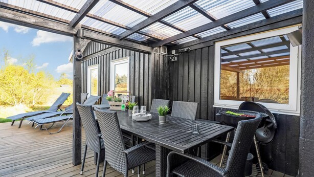 Eine überdachte Terrasse mit Tisch, Stühlen, einem Grill und Blick ins Grüne.