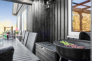 An outdoor patio with a grill, wicker chairs, and a table with drinks and a flower vase.