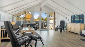 A spacious loft-style room with a high ceiling, large windows, a dining area, and a television. - Renovated holiday home with 4 bedrooms 800 meters from the North Sea. (Thisted)