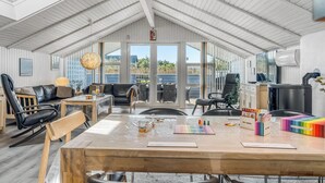 A spacious room with a high ceiling, a large table, and a view through the glass doors. - Renovated holiday home with 4 bedrooms 800 meters from the North Sea. (Thisted)