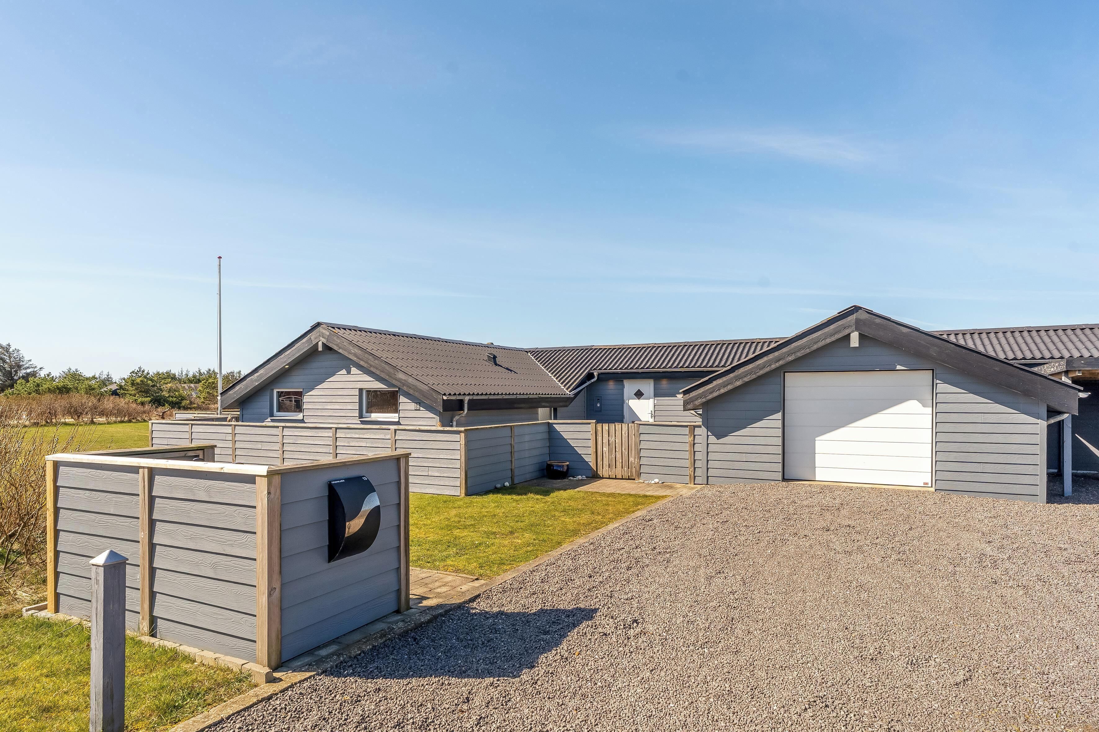 A row of single-story buildings with attached garages, a gravel driveway, and a fenced area.