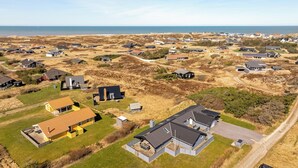An aerial view of a residential area with houses, a road, and a body of water in the background. - Renovated holiday home with 4 bedrooms 800 meters from the North Sea. (Thisted)