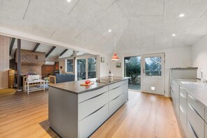 Una cocina moderna con una isla central, un comedor con pared de ladrillo y ventanas amplias.