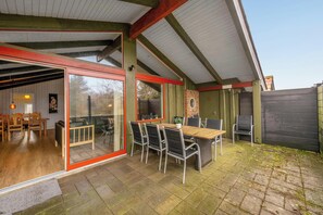 A patio with a wooden table and chairs, a glass door leading to an interior space, and a brick wall.