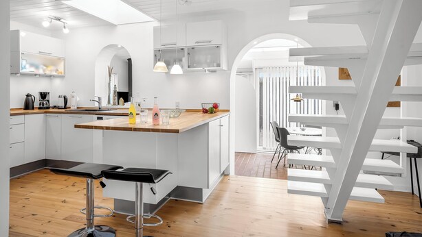 A modern kitchen with white cabinetry, a central island with bar stools, and a staircase with a unique design.
