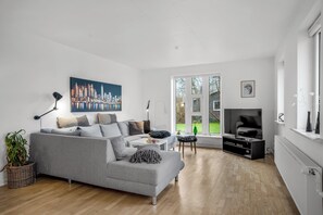 Een moderne woonkamer met een grijze bank, een flatscreen televisie en een stadsgezicht schilderij.