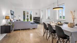 A modern living room with a grey sofa, a dining table with chairs, and a TV.