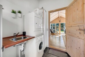 A compact kitchen with a washing machine, a sink, and two potted plants. - Lovely holiday home with sauna, spa and covered terrace (Lodbjerg Hede)
