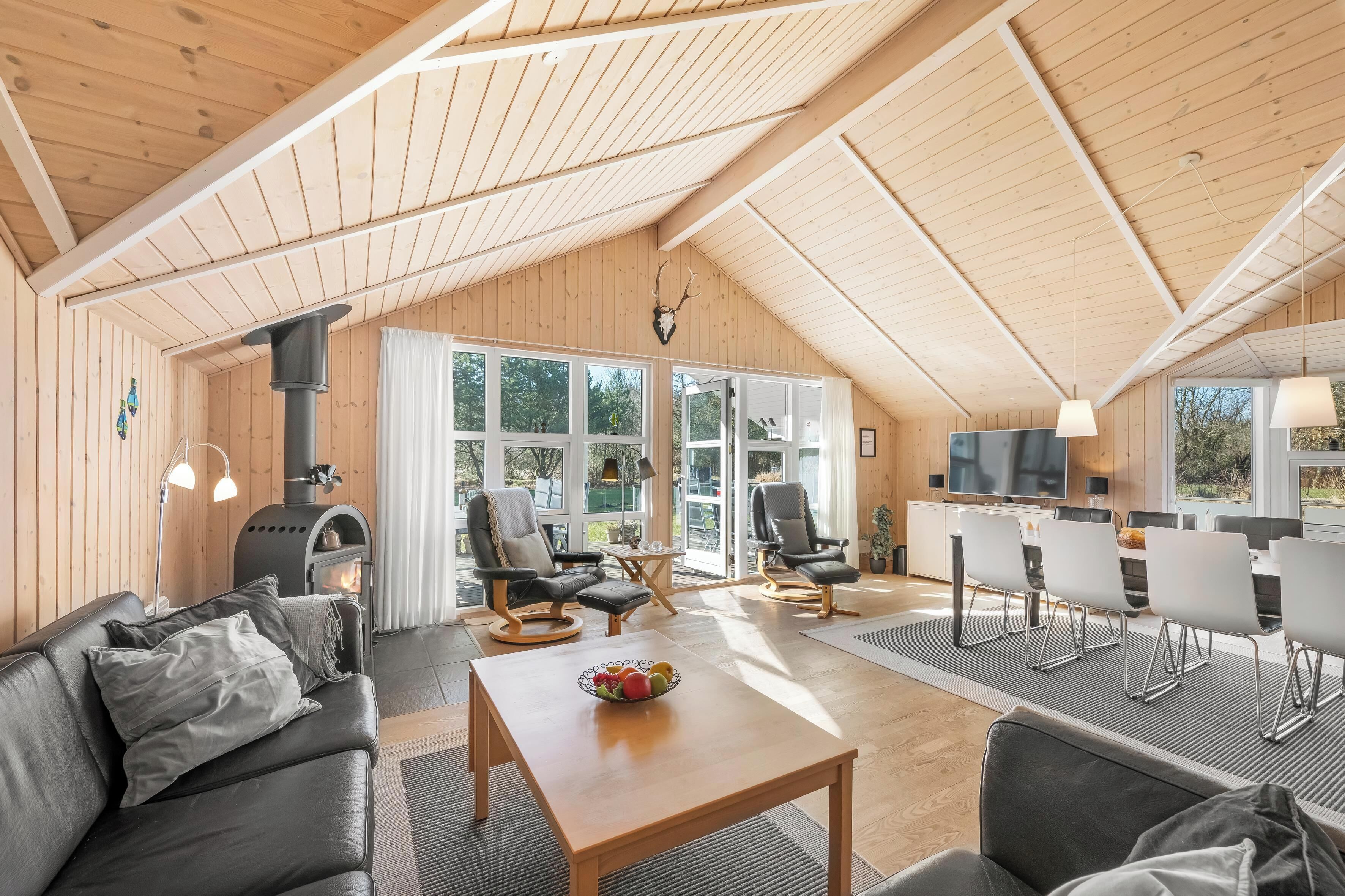 Un vaste espace de vie doté d’un plafond en bois, d’une cheminée, de meubles modernes et de grandes fenêtres.