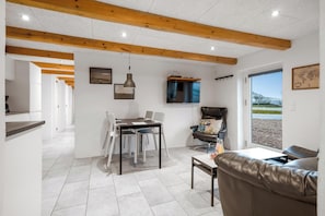 A modern living room with a dining area, wooden ceiling beams, a TV, and a view through a large window. - 16-person holiday home with view over the water and wilderness bath. (Thisted)