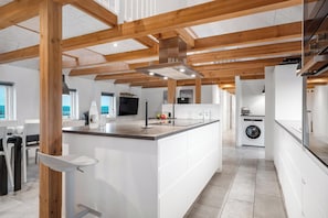 A modern kitchen with wooden beams, a central island, and a washing machine in the background. - 16-person holiday home with view over the water and wilderness bath. (Thisted)