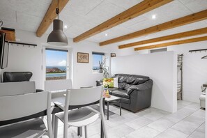 A modern living room with a dining area, a leather sofa, a table with chairs, a hanging pendant light, and a view of the sea through a window. - 16-person holiday home with view over the water and wilderness bath. (Thisted)