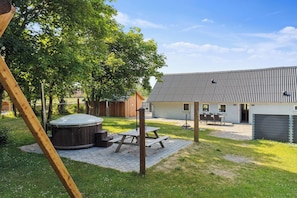 A backyard with a hot tub, picnic table, and a house with a metal roof. - 16-person holiday home with view over the water and wilderness bath. (Thisted)