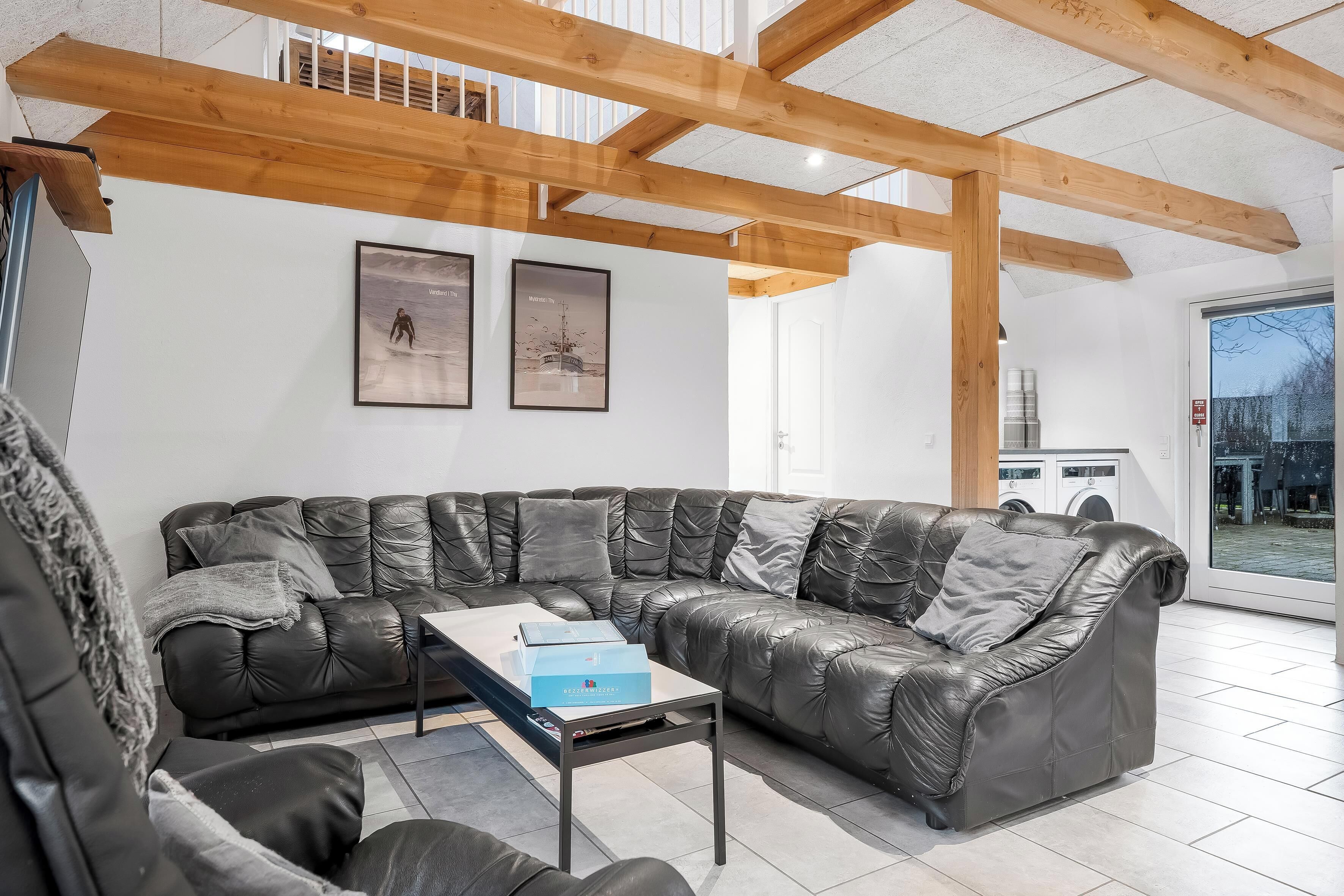 A modern living room with a leather sectional sofa, a coffee table, and wooden beams on the ceiling.