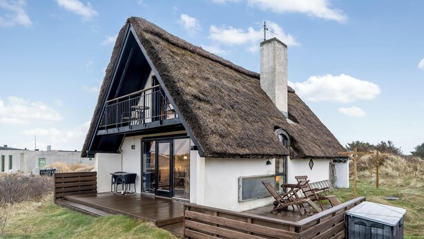Una casa con techo de paja, un balcón, una terraza y un pequeño espacio con mobiliario exterior.