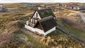 Casa con techo de paja y balcón, rodeada de un paisaje rural con otras viviendas.